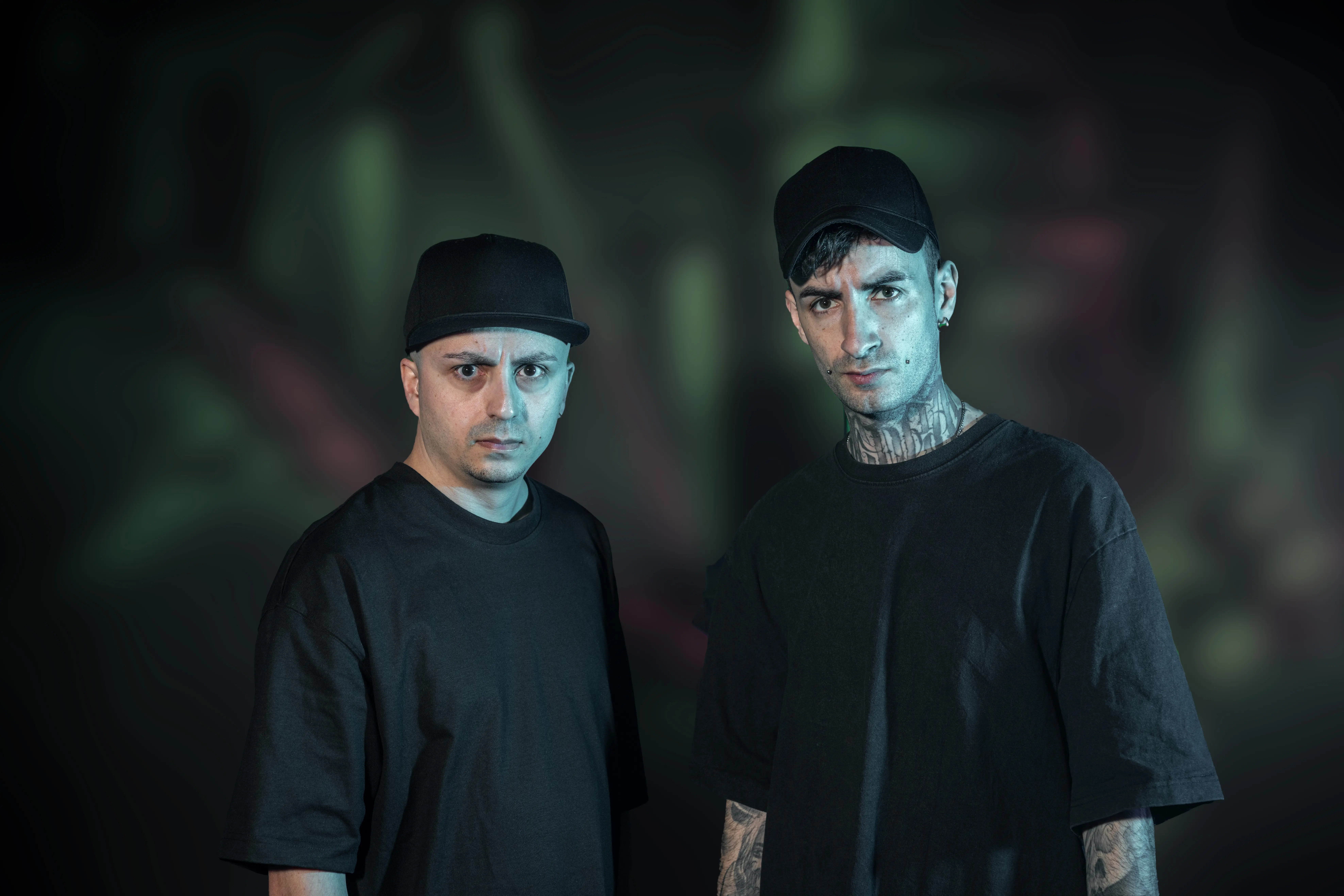 DJ Alien T and Nightshift looking at the camera posing in front of a dark decorated background